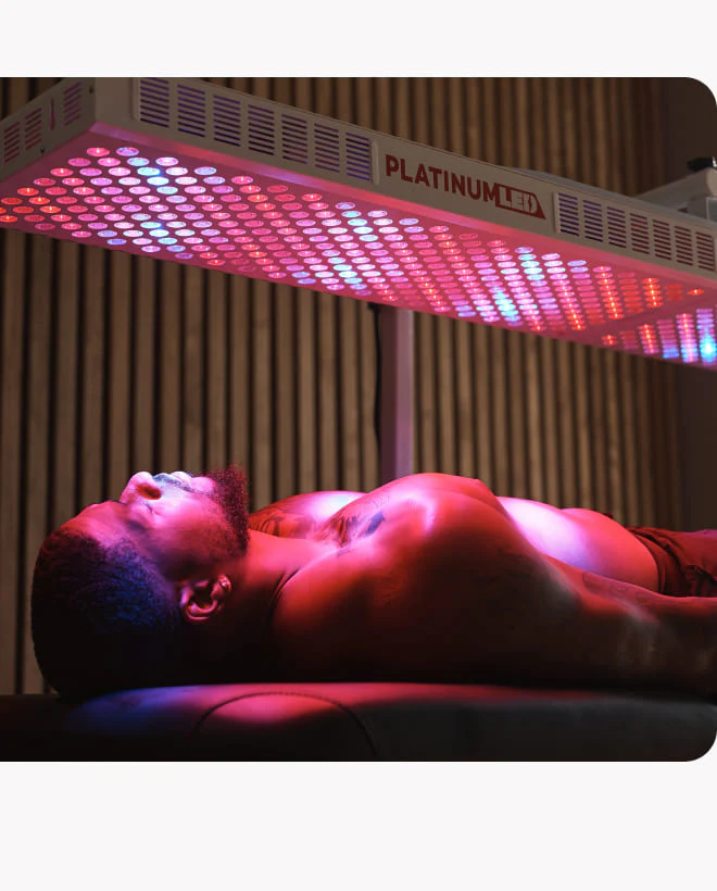 Client relaxing beside a full-body PlatinumLED BIOMAX 900 red light therapy panel at a Victory Health & Wellness clinic